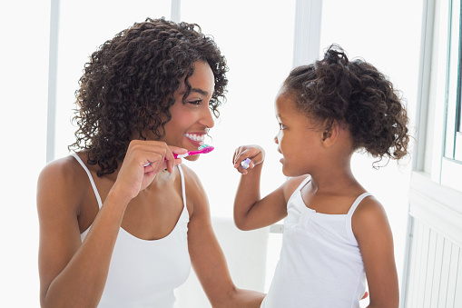 Mother and daughter practicing good dental hygiene by brushing together at the sink.