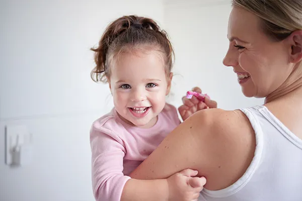 Mother teaching happy girl dental hygiene, baby toothbrush and mom holding kid.