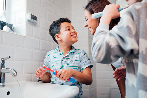 Woman helping her children brush their teeth