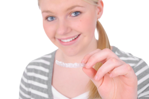 a smiling teen girl holding a clear aligner