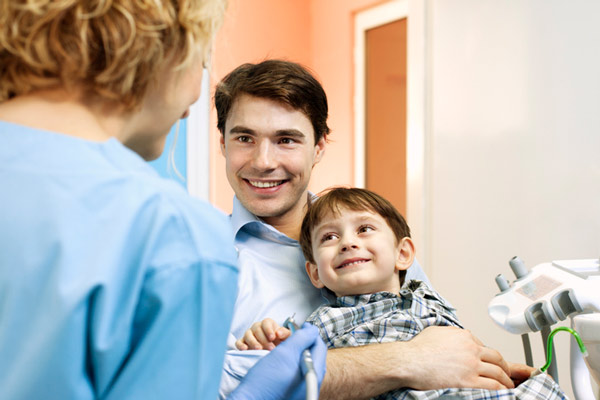 Two year old boy sitting on his dad's lap for dental exam.