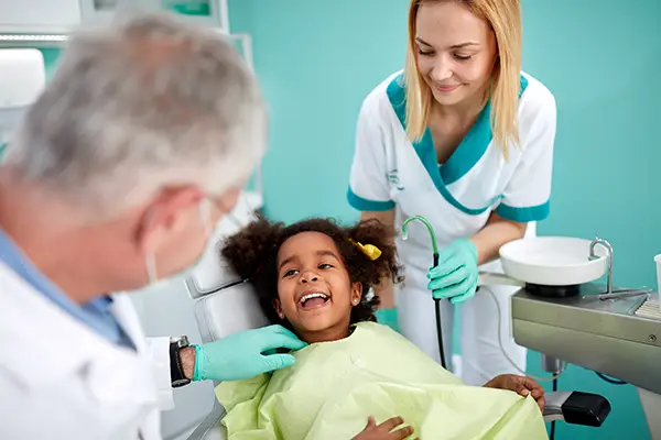 Adorable and young Black girl sitting in a dental chair and smiling at her dentist and assistant.