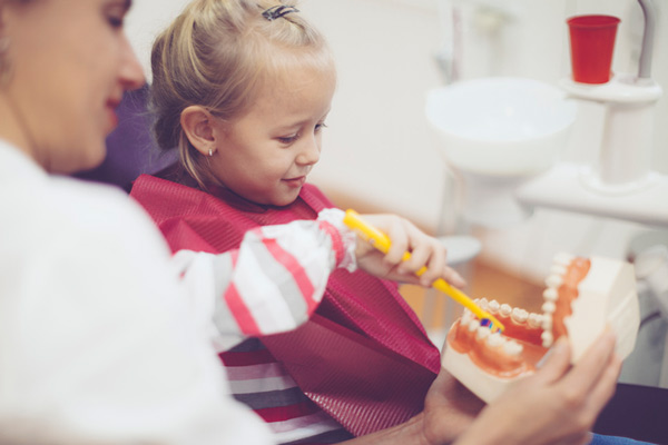 Young girl practicing brushing teeth with dentist watching.