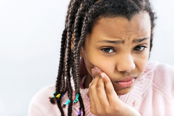 Young girl holding her cheek due to a tooth ache.