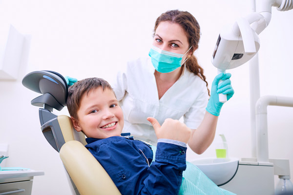 Child sitting in dental chair with doctor and giving a thumbs up at NC Pediatric Dentistry