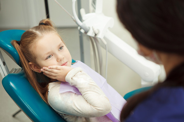 Young person with pigtails holding their cheek due to an aching tooth.