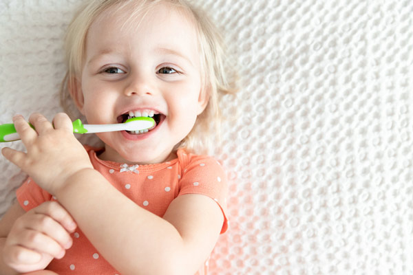 Happy little girl laying on bed and brushing her teeth