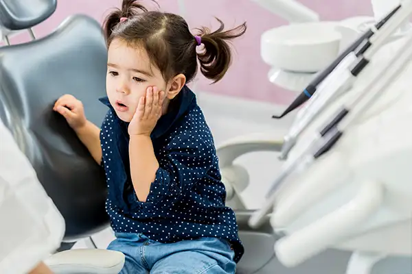 Young girl holding her cheek in discomfort while sitting in a dental chair, indicating a potential cavity.