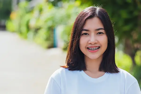 Smiling teenager with braces outdoors, showcasing confidence during orthodontic treatment.