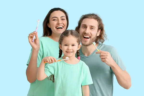 A little girl with her parents smiling and brushing their teeth together.