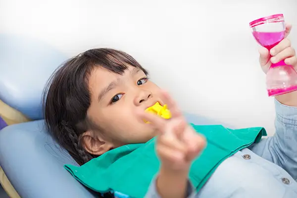 A young girl holding a timer while she patiently waits with a fluoride tray in her mouth.