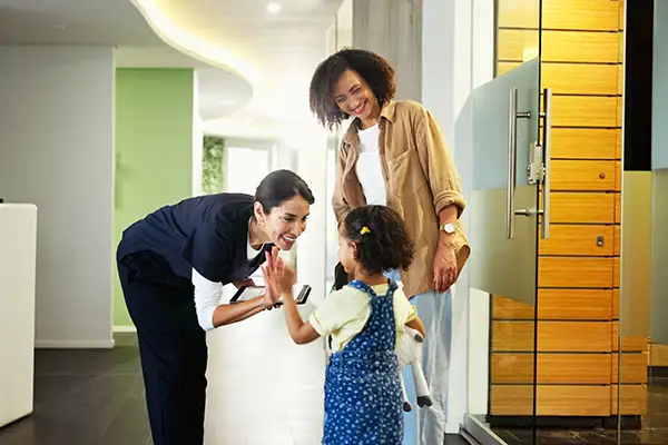 A happy dental hygienist high-fives a young patient right after she and her smiling mother enter the dental office.