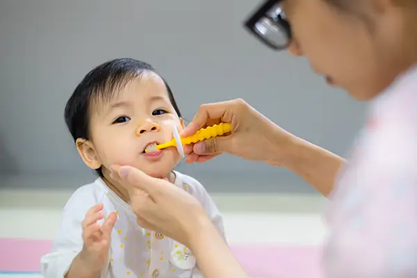Parent using a small toothbrush to clean their baby's teeth, highlighting proper dental care for infants.