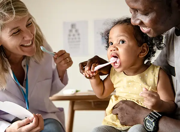 Family helping their baby learn how to brush teeth, with a dentist offering guidance on early oral care for infants.