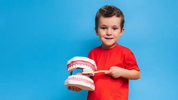 A young boy demonstrates how to brush his teeth on an oversized dental mouth model.