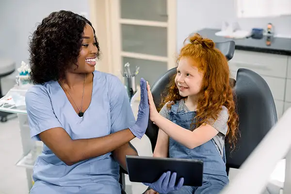 A smiling young girl and her dentist high-fiving each other after a successful and fun dental visit.