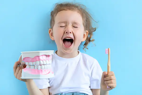 An ecstatic little girl holding an oversized toothbrush and mouth model, excited about dental care.