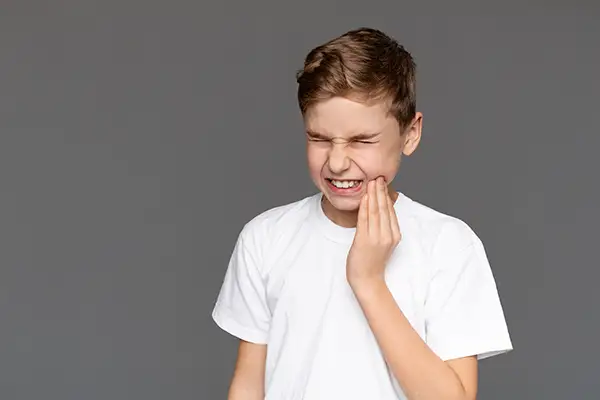 Young boy grimacing in pain while holding his jaw, highlighting the urgency of addressing a dental emergency.