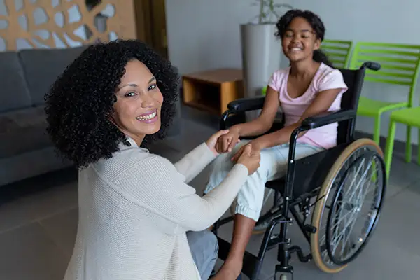A smiling mom with her daughter sitting in a wheelchair, waiting for an appointment in the reception area.