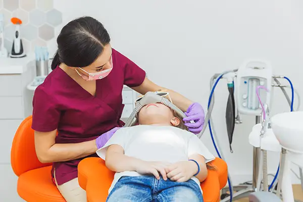 Dentist administering sedation to a child patient using a nitrous oxide mask during a dental procedure.