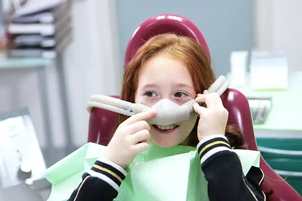 Smiling child wearing a nitrous oxide mask to receive sedation before a dental procedure.