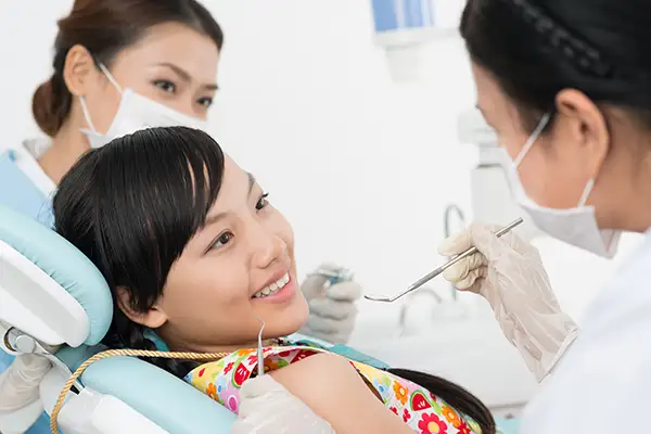 Young girl smiling during a preventive dental exam as the dentist and dental assistant provide care in a friendly environment.